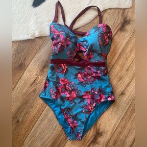 Basta Surf one-piece swimsuit with a teal background and a pink floral pattern
